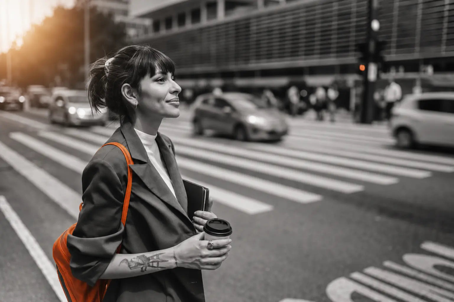 woman walks across street holding coffee and orange bag